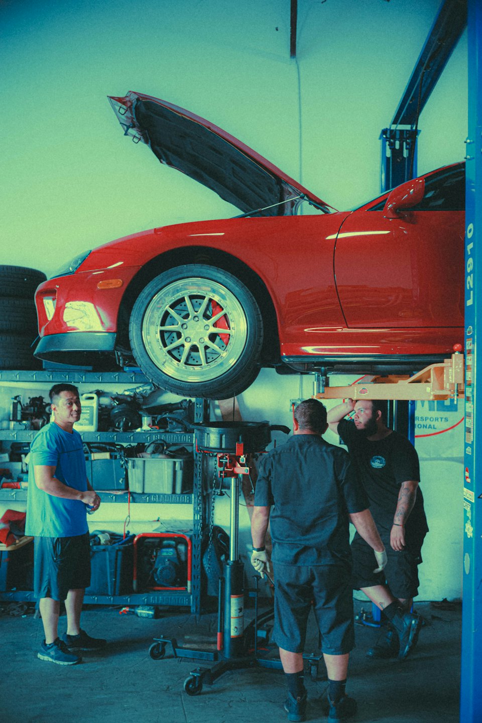 Mechanics looking at an open-hood sports car in a shop.